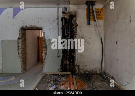 Ein teilweise abgerissener Innenraum mit freiliegenden Ziegelwänden, sichtbaren Rohrleitungen, verstreuten Trümmern und einem gelben Sicherheitsschild an der Wand. Stockfoto