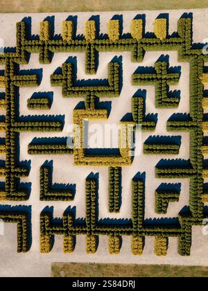 Aus der Vogelperspektive eines Heckenlabyrinths mit symmetrischen Mustern, leichten Kieswegen und einer quadratischen Einhausung, umgeben von Gras in einer Gartenanlage Stockfoto