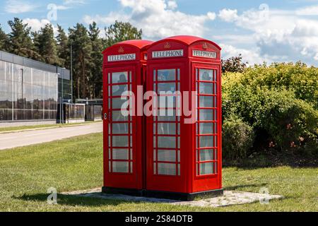 Zwei rote britische Telefonzellen auf einem gepflasterten Bereich mit Gras, ein modernes Glasgebäude, Bäume, Büsche und ein blauer Himmel mit verstreuten Wolken. Stockfoto