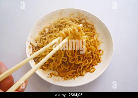 Halten Sie die Essstäbchen mit der Hand, um scharfe Instant-Nudeln auf dem Teller zu essen Stockfoto