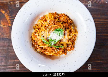 Eine köstliche Portion Spaghetti, garniert mit einer reichhaltigen Fleischsauce und garniert mit frischem Basilikum. Dieses Gericht wird auf einer einfachen weißen Tafel präsentiert Stockfoto