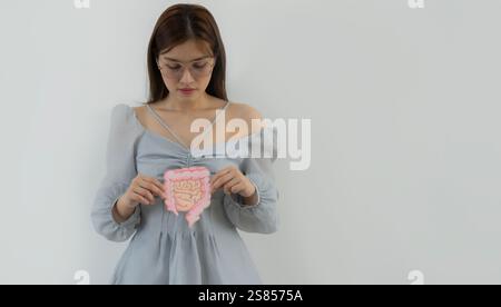 Portraitbild einer jungen asiatischen Frau, die Darmform hält und glücklich über weißen Wandhintergrund mit Kopierraum blickt. Stockfoto