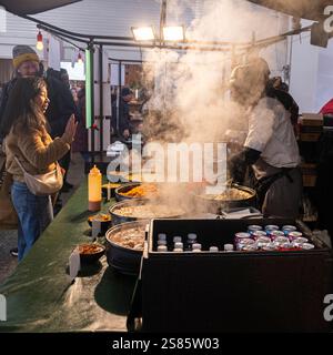 Leute, die in einem dampfenden, geschäftigen Brick Lane Street Food Outlet serviert werden Stockfoto