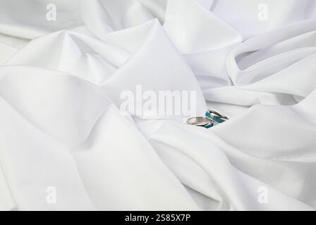 Eheringe mit türkisfarbener Intarsie werden auf weißer Seide gelegt und symbolisieren Reinheit und Engagement. Stockfoto