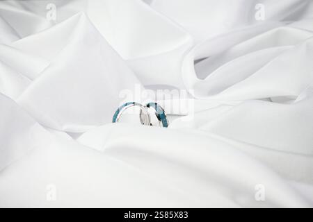 Eheringe mit türkisfarbener Intarsie werden auf weißer Seide gelegt und symbolisieren Reinheit und Engagement. Stockfoto