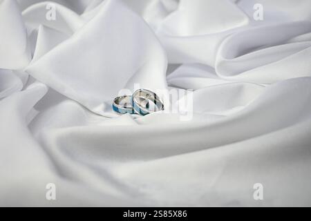 Eheringe mit türkisfarbener Intarsie werden auf weißer Seide gelegt und symbolisieren Reinheit und Engagement. Stockfoto