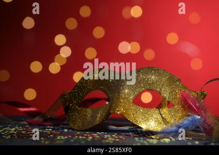 Schöne Karnevalsmaske und Konfetti auf farbigem Hintergrund mit verschwommenen Lichtern, Nahaufnahme Stockfoto