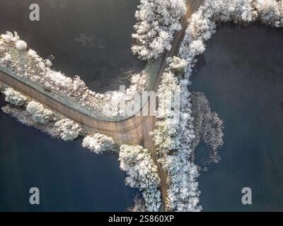 Eine wunderschöne Vogelperspektive zeigt eine frostige Winterlandschaft mit schneebedeckten Bäumen entlang einer unbefestigten Straße, umgeben von gefrorenen Seen, die Natu betont Stockfoto