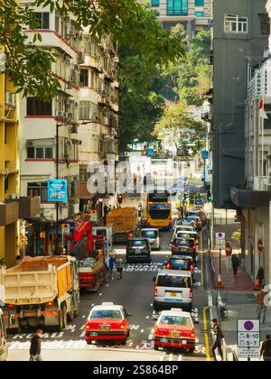 Hongkong, China - 21. Januar 2025 : Eine belebte Straßenszene in der Stadt, voll mit Fahrzeugen wie Taxis, Bussen und Lastwagen. Hohe Gebäude säumen das n Stockfoto
