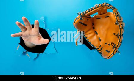 Menschliche Hand, die Softball- oder Baseballhandschuhe durch gerissenes Papier trägt. Modellerstellung oder Kopierbereich. Sportbegriff Stockfoto