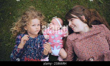 Familienverbindung mit Mutter, Schwester, die sich in der Nähe des Neugeborenen befindet, sich auf grünem Gras entspannen und eine zärtliche Verbindung teilen Stockfoto