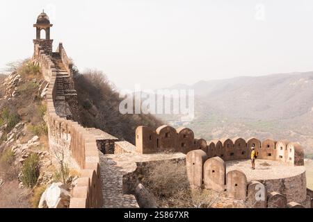 Mann in gelbem Hemd genießt Sonnenaufgang an den Stadtmauern von Jaipur in Rajasthan, Indien. Frühmorgendliches Licht auf den trüben Bergen und der Festungsmauer Stockfoto
