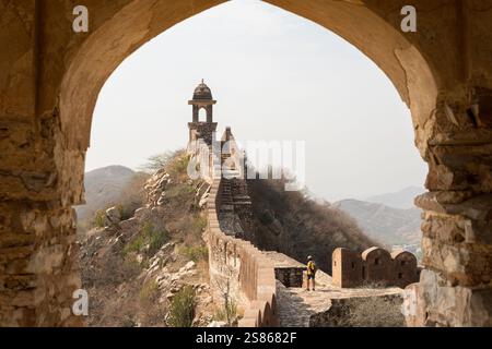 Mann in gelbem Hemd genießt Sonnenaufgang an den Stadtmauern von Jaipur in Rajasthan, Indien. Frühmorgendliches Licht auf den trüben Bergen und der Festungsmauer Stockfoto