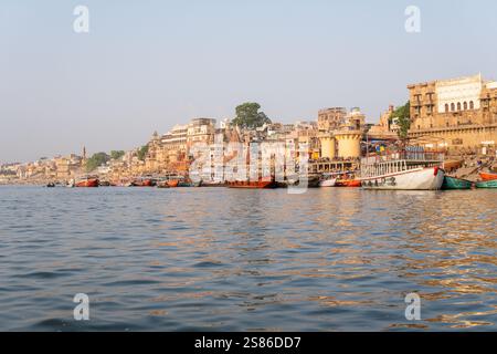 VARANASI, INDIEN - 11. APRIL 2024: Blick auf den Sonnenuntergang über die antike Stadt Varanasi mit alten Booten und dem Wasser des Ganges im Vordergrund Stockfoto