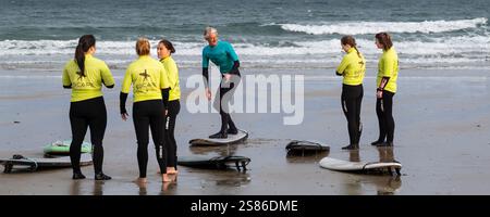Ein Panoramabild eines Surflehrers von der Escape Surfing School, der eine Surfstunde mit einer Gruppe weiblicher Lerner am Towan Beach in ne hält Stockfoto