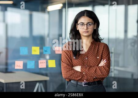 Porträt einer erfolgreichen selbstbewussten Geschäftsfrau, Büroangestellten mit überkreuzten Armen, die in die Kamera schauen. Zufriedene und ernste Frau im Büro am Arbeitsplatz. Stockfoto
