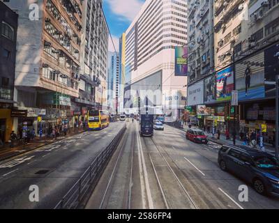 Hongkong, China - 21. Januar 2025 : Eine lebhafte Straßenszene voller Aktivität. Hohe Gebäude säumen eine Straße mit Straßenbahnen und verschiedenen Fahrzeugen. A Stockfoto