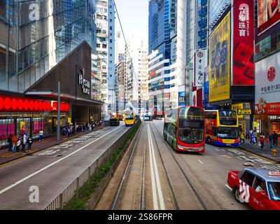 Hongkong, China - 21. Januar 2025 : Eine belebte Straßenszene, von einer Straßenbahn aus gesehen, zeigt hochaufragende Wolkenkratzer, lebhafte Werbung und Busse Stockfoto