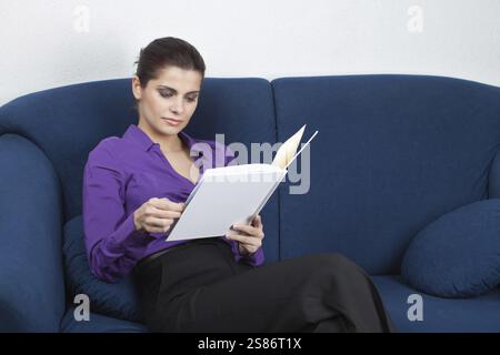 Junge, hübsche Geschäftsfrau, die im Wartezimmer auf dem Sofa sitzt und ein Album aufräumt, Belgien, Europa Stockfoto