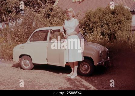 1960er Jahre, Sommer und eine junge Frau neben ihrem Goggomobil, einem zweitürigen Kleinwagen mit Heckmotor, hergestellt von Hans Glas in Bayern. Die hier vorgestellte Version, der Glas Goggomobile 250 (T250), hatte ursprünglich nach hinten aufklappbare Türen, ein Merkmal im Fahrzeugdesign, das früher häufig verwendet wurde, aber aus Sicherheitsgründen geändert wurde. Der Motor des Goggomobil wurde 1954 erstmals auf der IFAM Fahrrad- und Motorradmesse gesehen und war ein luftgekühlter Zweitaktmotor mit ursprünglich 250 ccm Hubraum. Diese Kleinwagen, auch bekannt als „Minicars“, wurden in den späten 1940er und 1950er Jahren erstmals als Dreiräder hergestellt. Stockfoto
