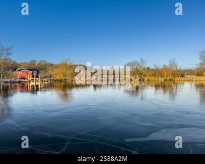 Gefrorener See auf der Pool Bridge Farm mit einer Saunahütte mit Blick auf das eisbedeckte Wasser an einem hellen, sonnigen Wintermorgen. York. UK Stockfoto
