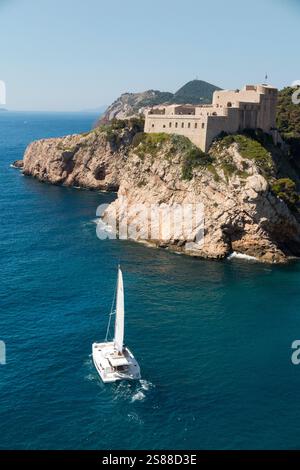 Die italienische Fortezza di San Lorenzo, oft auch „Dubrovnik's Gibraltar“ genannt, ist eine Festung und ein Theater außerhalb der ummauerten Altstadt/Altstadt von Dubrovnik, erbaut auf hervorragenden Felsvorsprüngen mit steilen Klippen, Fort Lovrijenac oder Festung St. Lawrence. Kroatien. Ein teures Yachtboot fährt entlang der Küste vorbei an der Burg. (138) Stockfoto