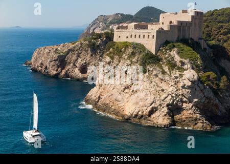 Die italienische Fortezza di San Lorenzo, oft auch „Dubrovnik's Gibraltar“ genannt, ist eine Festung und ein Theater außerhalb der ummauerten Altstadt/Altstadt von Dubrovnik, erbaut auf hervorragenden Felsvorsprüngen mit steilen Klippen, Fort Lovrijenac oder Festung St. Lawrence. Kroatien. Ein teures Yachtboot fährt entlang der Küste vorbei an der Burg. (138) Stockfoto