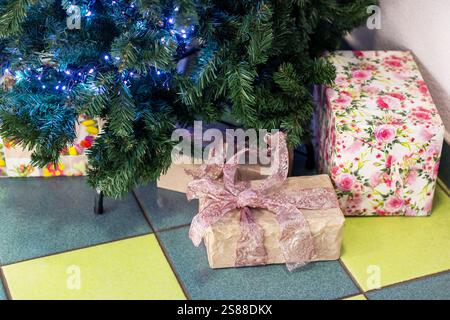 Wunderschön gewickelte Weihnachtsgeschenke, die mit bunten Bändern verziert sind, werden unter einem atemberaubenden Weihnachtsbaum platziert, der mit funkelnden blauen Lichtern geschmückt ist Stockfoto