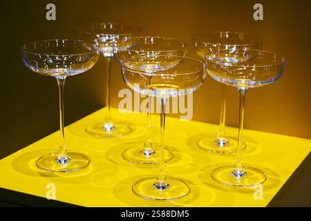 Sechs elegant gestaltete Sektgläser sind sorgfältig auf einer leuchtend gelben Oberfläche angeordnet und schaffen ein optisch ansprechendes Design für jeden Anlass Stockfoto