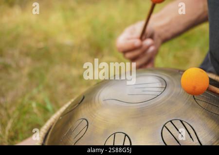 Ein junger Mann spielt die Handpfanne. Eine Szene mitten im Wald. Der klangliche Klang eines Xylophons wird mit der Melodie des Raumes assoziiert. Stockfoto