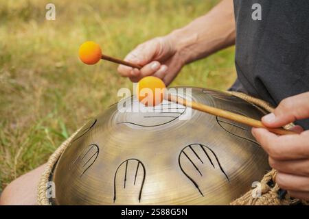 Ein junger Mann spielt die Handpfanne. Eine Szene mitten im Wald. Der klangliche Klang eines Xylophons wird mit der Melodie des Raumes assoziiert. Stockfoto