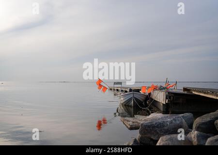 Kleines Fischerboot mit Netzflaggen am Pier. Angelboot Pier und Boot am Meer am Abend. Sonnenuntergang über dem Meer mit einem Holzsteg Stockfoto