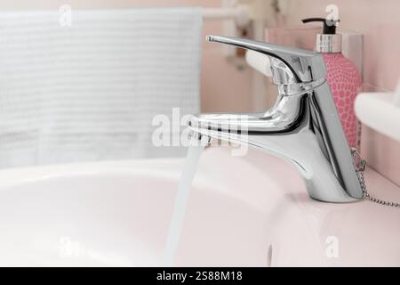 Wasserhahn mit Wasserstrahl und verschwommenen Accessoires im Badezimmer. Stockfoto