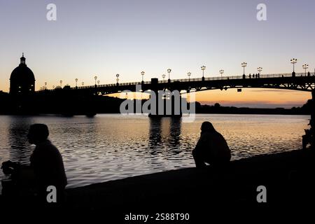 Stimmungsvoller Sonnenuntergang auf die Brücke Pont Saint-Pierre in Toulouse, Frankreich, mit ihren berühmten Straßenlaternen. Silhouetten von sitzenden Menschen. Stockfoto