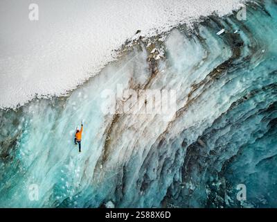 Luftaufnahme eines Athleten in orangefarbener Jacke Eisklettern an der großen gefrorenen Eiswand des Bogdanovich-Gletschers im Bergtal in Kasachstan Stockfoto