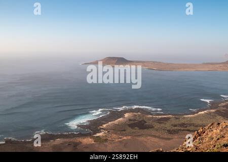 Blick von einer Klippe auf die Küste und den Atlantischen Ozean. Land der Insel La Graciosa im Hintergrund. Blauer Abendhimmel mit einem Hauch Rosa. Mirador de GUI Stockfoto