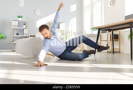 Junger, ungeschickter Mann, der auf den Boden fällt und sich zu Hause oder im Büro den Arm verletzt. Stockfoto