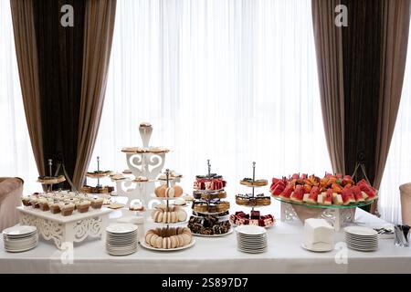 Ein wunderschön gestalteter Desserttisch bietet eine Vielzahl an süßen Leckereien, darunter Kuchen, Gebäck, Macarons und frisches Obst. Die Umgebung ist elegant Stockfoto