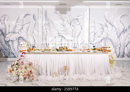 Ein üppig dekorierter Hochzeitsempfang bietet eine Auswahl an Desserts, Vorspeisen und ein wunderschönes Blumenarrangement. Der Hintergrund ist mit einem s versehen Stockfoto