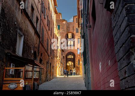 Man läuft die steile, enge Straße der Via della Galluzza hinunter, eine steile, enge Straße mit mittelalterlichen Bögen in Siena, Italien Stockfoto