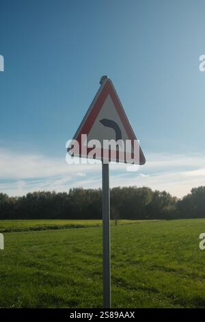 Ein dreieckiges Zeichen mit einem roten Pfeil, der nach rechts zeigt. Das Schild ist in einem grasbewachsenen Feld mit klarem blauem Himmel Stockfoto