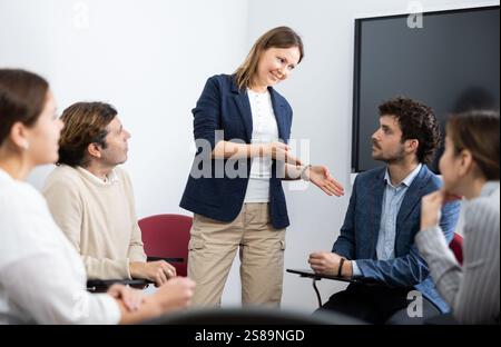 Positiv erfolgreiche Lehrerin, die Antworten von Schülern unterschiedlichen Alters hört, während sie im Kreis beim Fremdsprachenunterricht sitzt Stockfoto