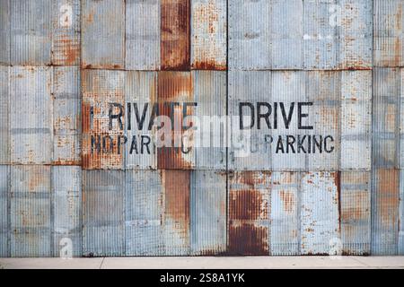 Blick auf verrostete alte Wellblechverkleidung mit den Worten „Private Drive“ und „No Parking“ abstrakte Textur Stockfoto