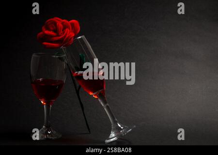 Negativer Raum zwei Weingläser, die sich gegenseitig tosten, und eine Rose, die auf beiden Seiten des Weinglases auf schwarzem Hintergrund steht, dunkelschwarzem Hintergrund Stockfoto