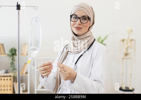 Selbstbewusste muslimische Ärztin, die Hijab trägt, bereitet intravenösen Tropfen in modernen Krankenhäusern vor. Nahöstliche Frau, Erwachsene, medizinische Fachkraft konzentriert auf die Patientenversorgung. Stockfoto