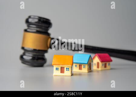 Ein Hammer und bunte Miniaturhäuser. Immobilienauktion oder Zwangsvollstreckung, Konzept des Immobilienrechts. Stockfoto