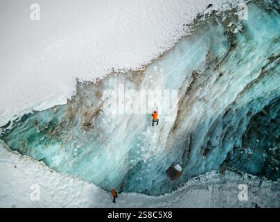 Luftaufnahme eines Athleten in orangefarbener Jacke Eisklettern an der großen gefrorenen Eiswand des Bogdanovich-Gletschers im Bergtal in Kasachstan Stockfoto