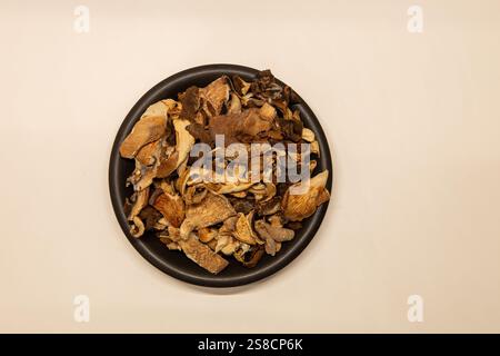 Verschiedene getrocknete Pilze auf einer dunklen Keramikplatte, isoliert auf weißem Hintergrund. Blick von oben. Stockfoto
