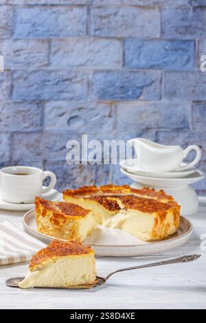 San Sebastian oder Basque verbrannte Käsekuchen Scheiben auf Teller und auf Kuchenschaufel auf weißem Holztisch mit einer Tasse Kaffee und Sahne im Hintergrund Stockfoto