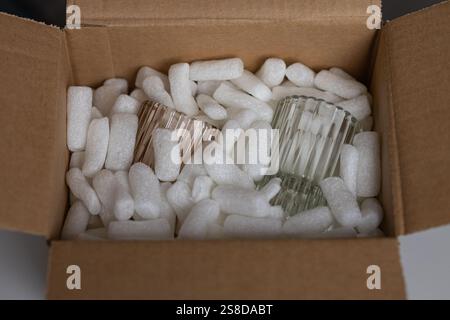 Umweltfreundlicher Karton gefüllt mit weißen biologisch abbaubaren Erdnüssen und zwei geriffelten Glasbechern. Sichere Versandmethoden für zerbrechliche Gegenstände Stockfoto